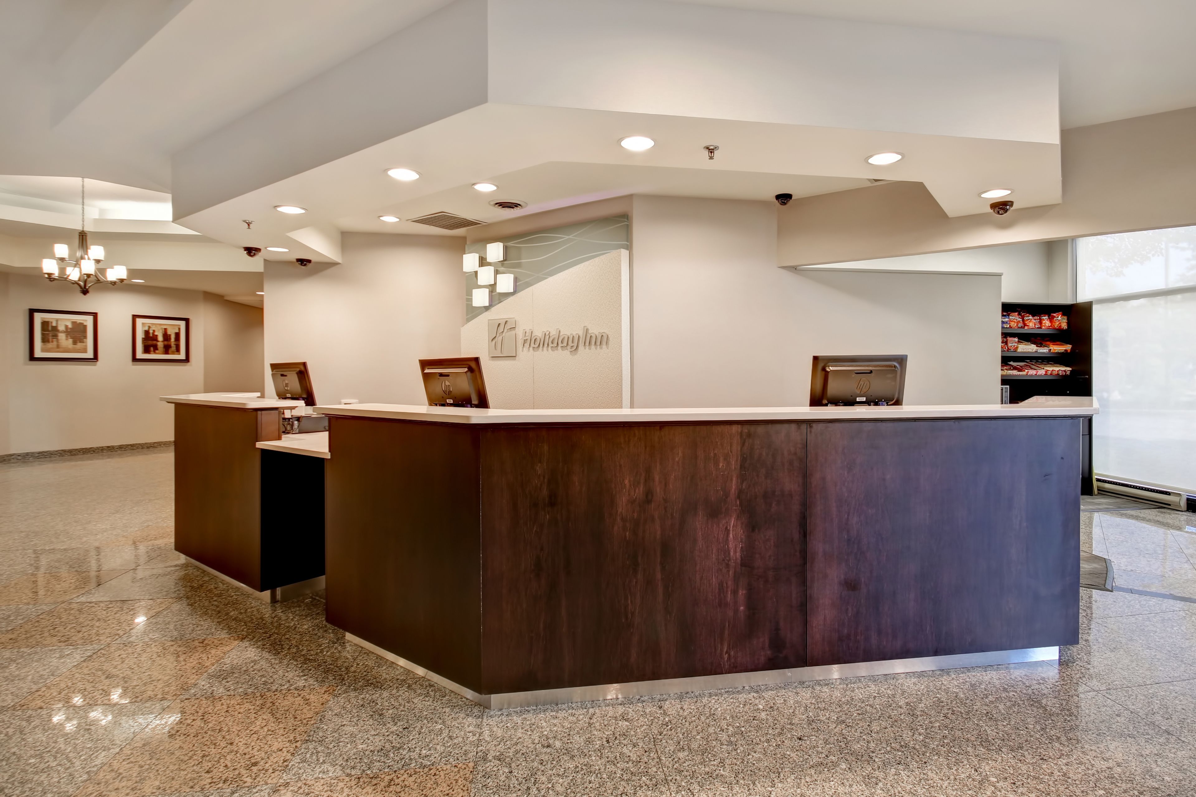 Uma receção com acabamento em madeira escura, um letreiro 'Holiday Inn' e um candeeiro moderno.