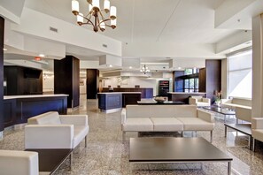 Un hall d'hôtel moderne avec un comptoir d'accueil, un espace salon et une cuisine en arrière-plan.