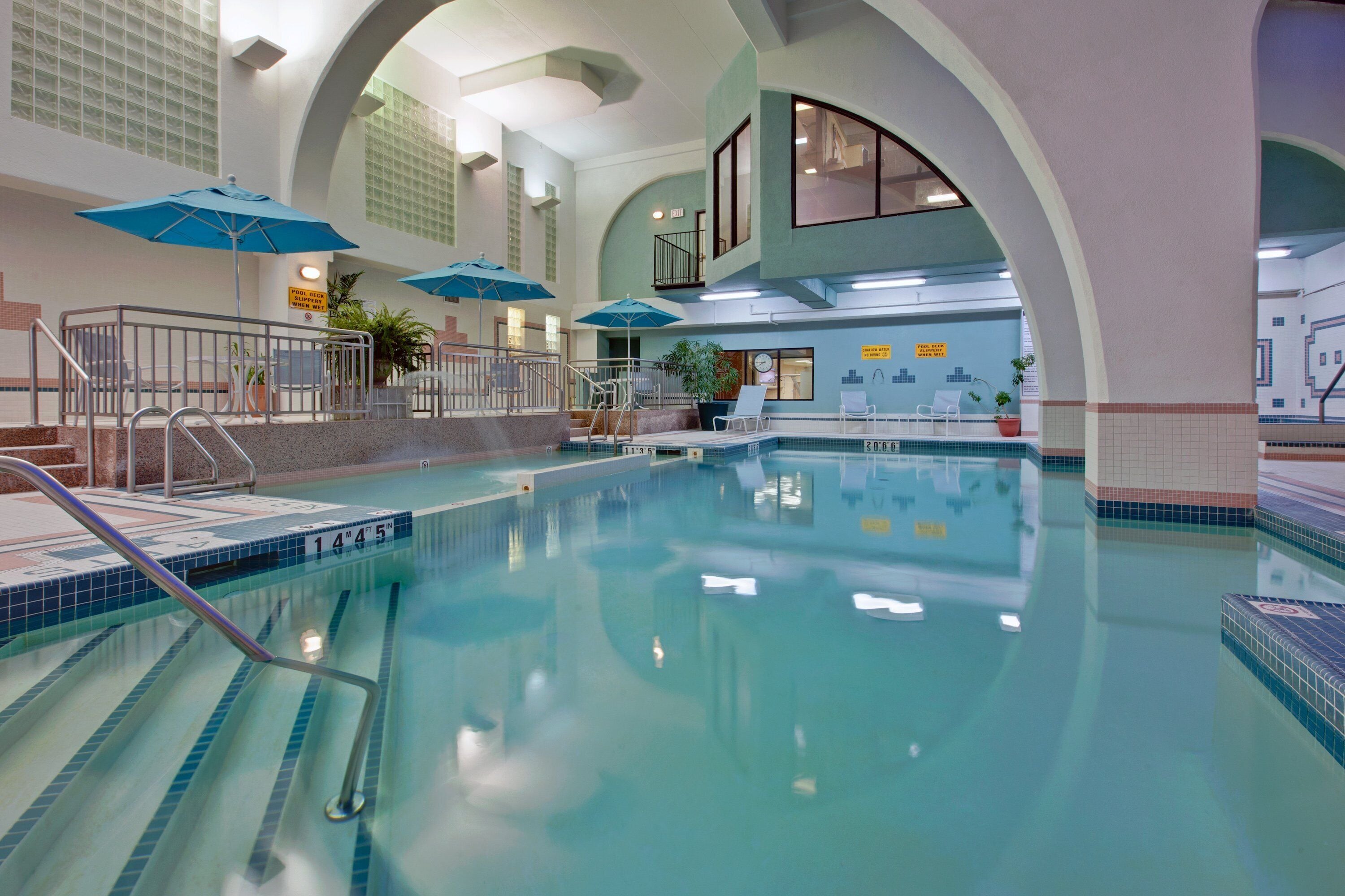 An indoor swimming pool with clear water, a diving board, and multiple umbrellas.
