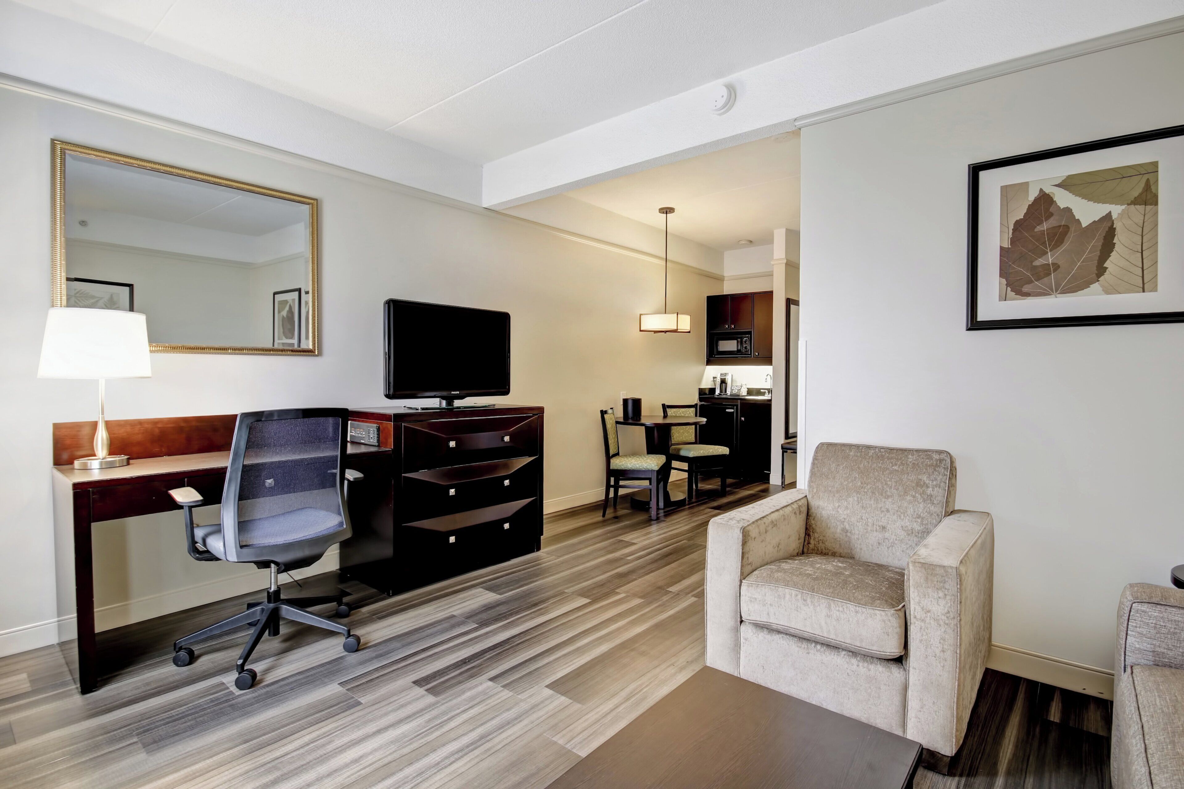 A hotel room with a desk, chair, television, and a sofa.