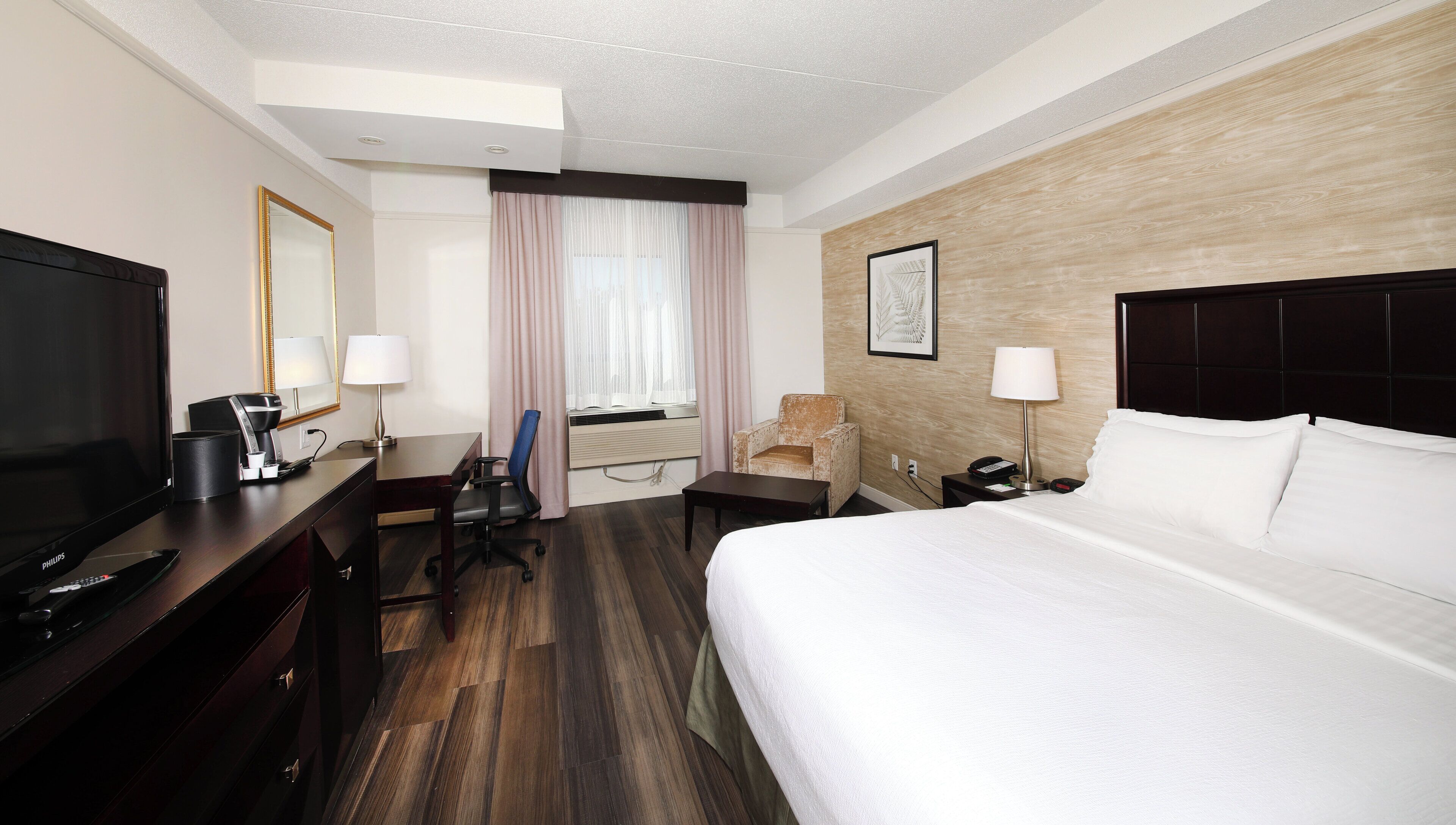 Ein Hotelzimmer mit Bett, Schreibtisch, Stuhl, Fernseher und Nachttisch mit Lampe.
