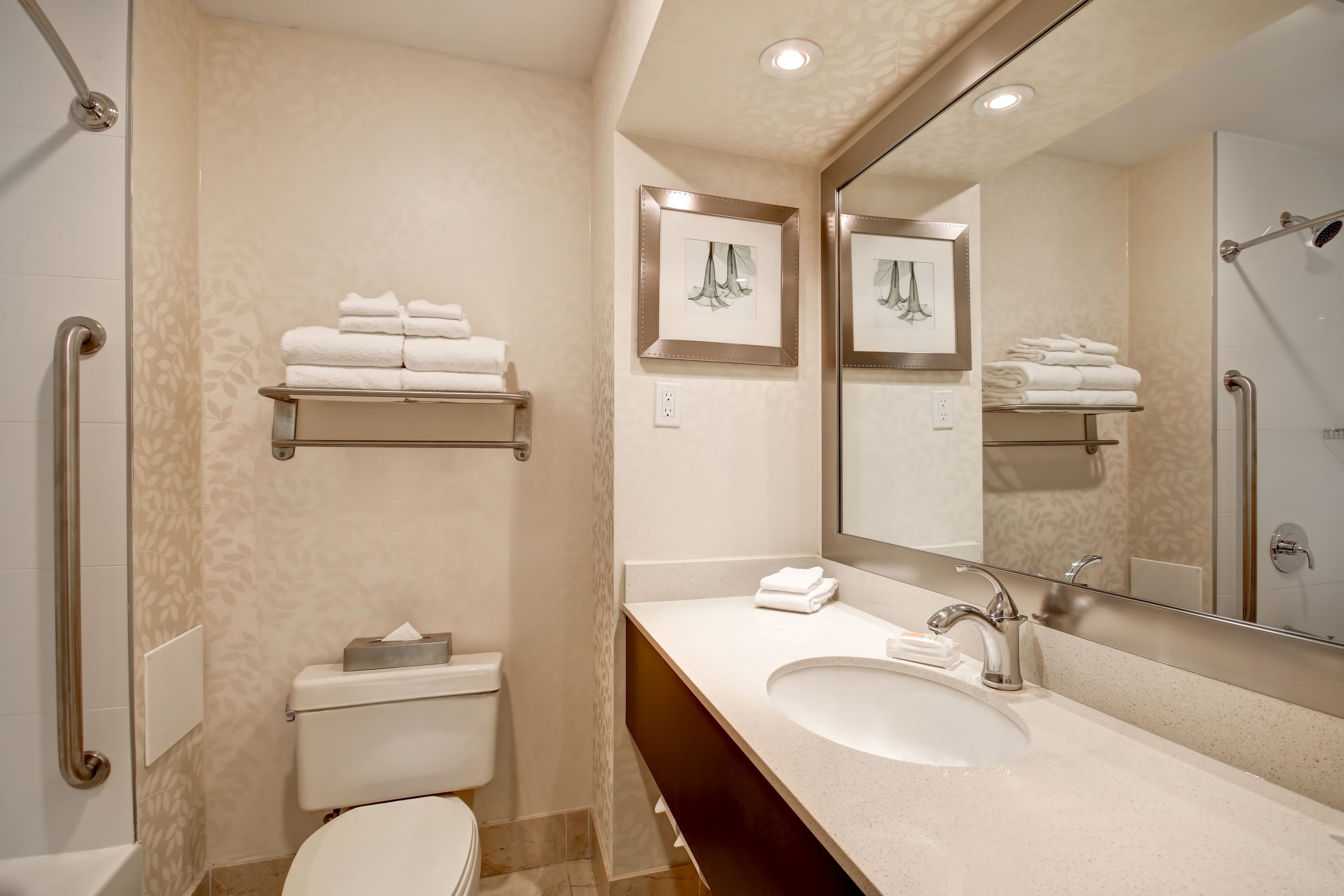 A modern bathroom with a toilet, sink, and shower. There are towels on a shelf and a mirror above the sink.