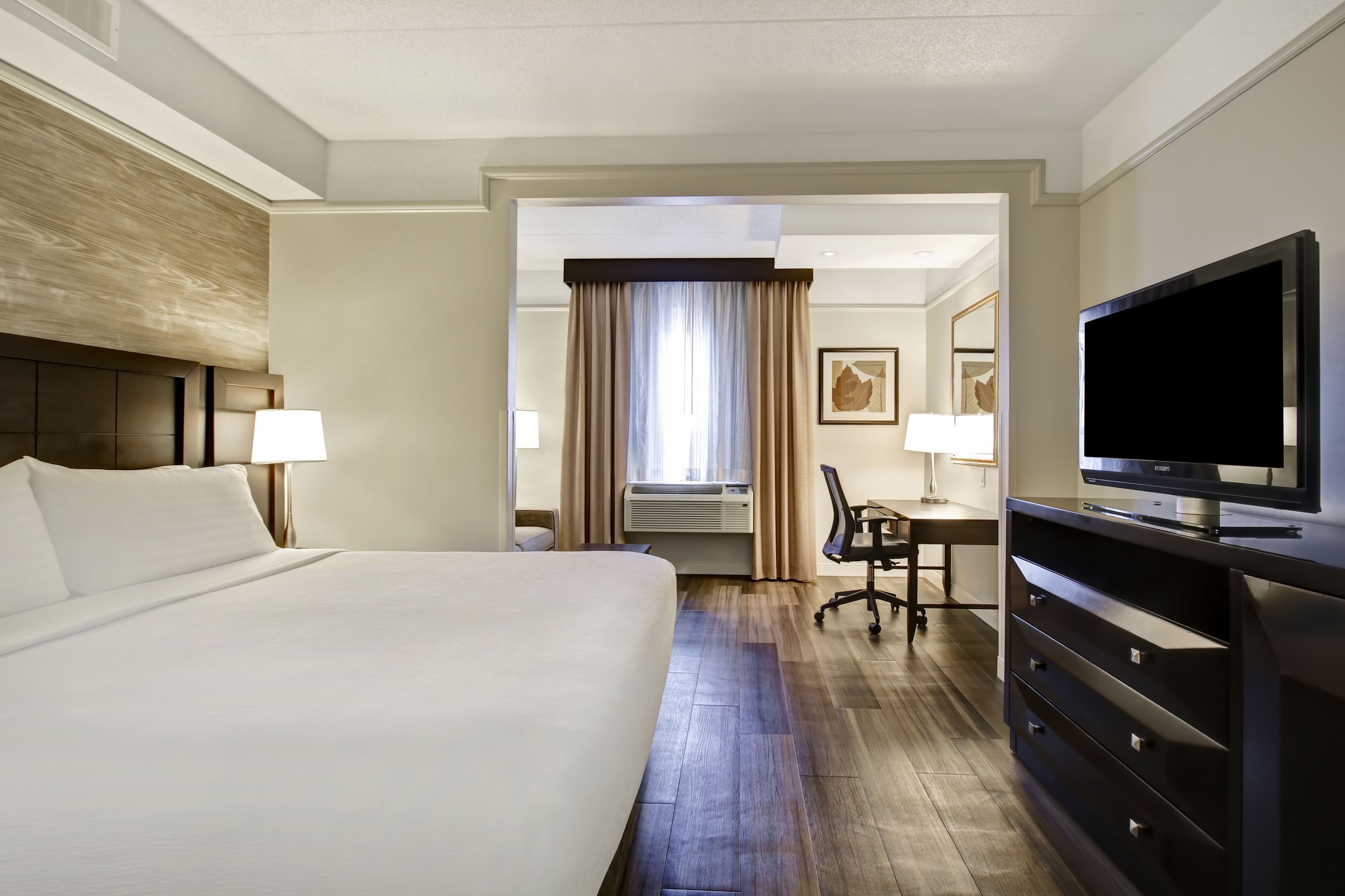 Habitación de hotel con una cama grande, un escritorio con silla, televisión y ventana con cortinas.