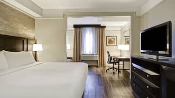 A hotel room with a large bed, a desk with a chair, a television, and a window with curtains.