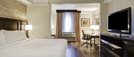 Habitación de hotel con una cama grande, un escritorio con silla, televisión y ventana con cortinas.
