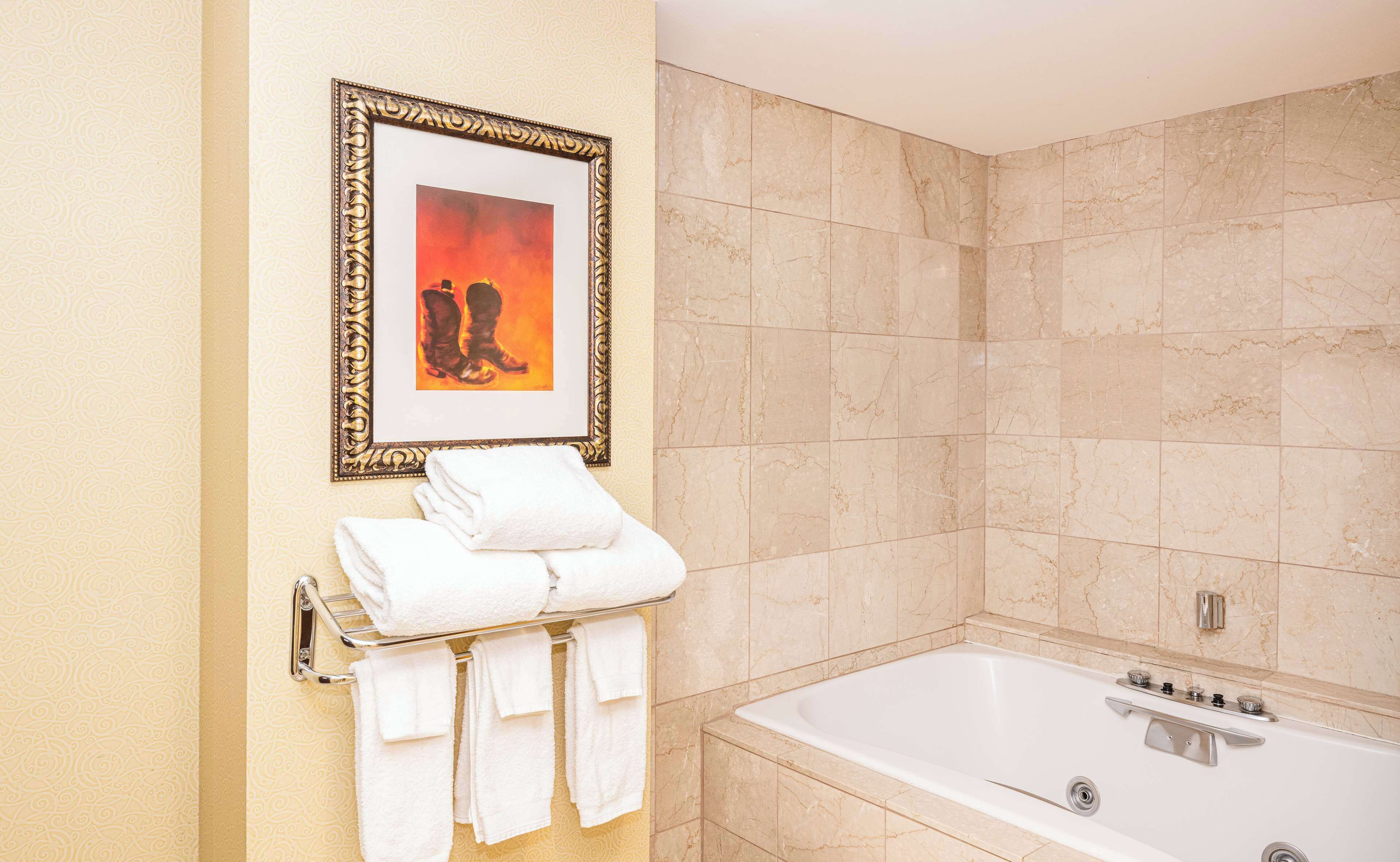 A bathroom with a marble-tiled wall, a framed picture, and a stack of white towels on a metal rack.