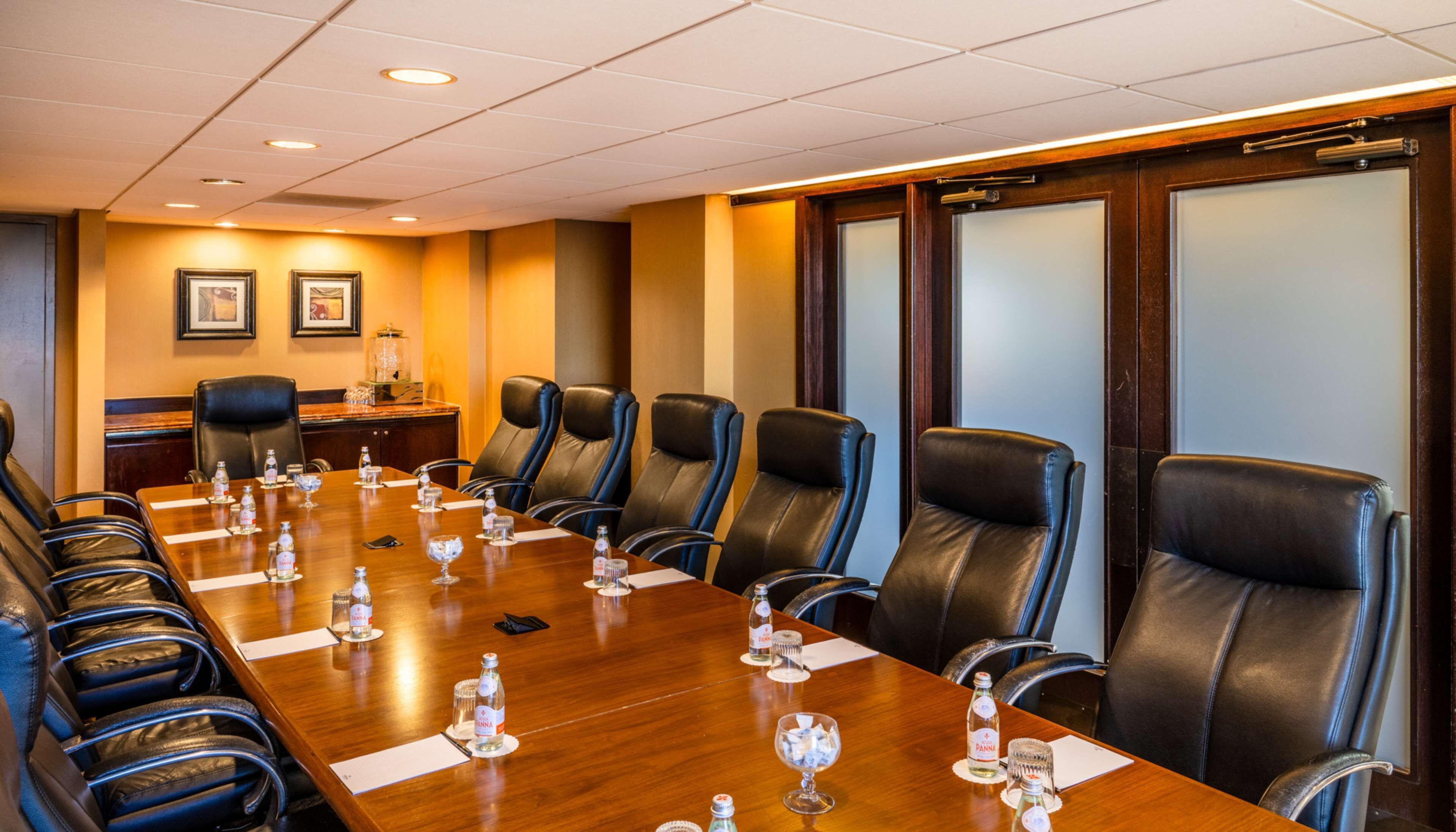 A conference room with a long wooden table, black leather chairs, and framed pictures on the wall.