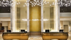 A hotel reception area with a modern design, featuring a central glass partition, two large reception desks, and a chandelier with multiple light fixtures. - Hilton Richardson Dallas (Richardson)