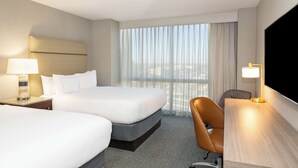 A hotel room with two beds, a desk, a chair, a TV, and a large window with curtains. - Hilton Richardson Dallas (Richardson)