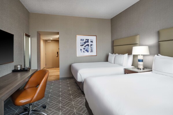 Two single beds with white linens, a desk, and flat-screen TV.