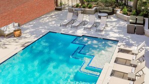 A swimming pool with a geometric design, surrounded by lounge chairs and a brick wall. - Hilton Richardson Dallas (Richardson)