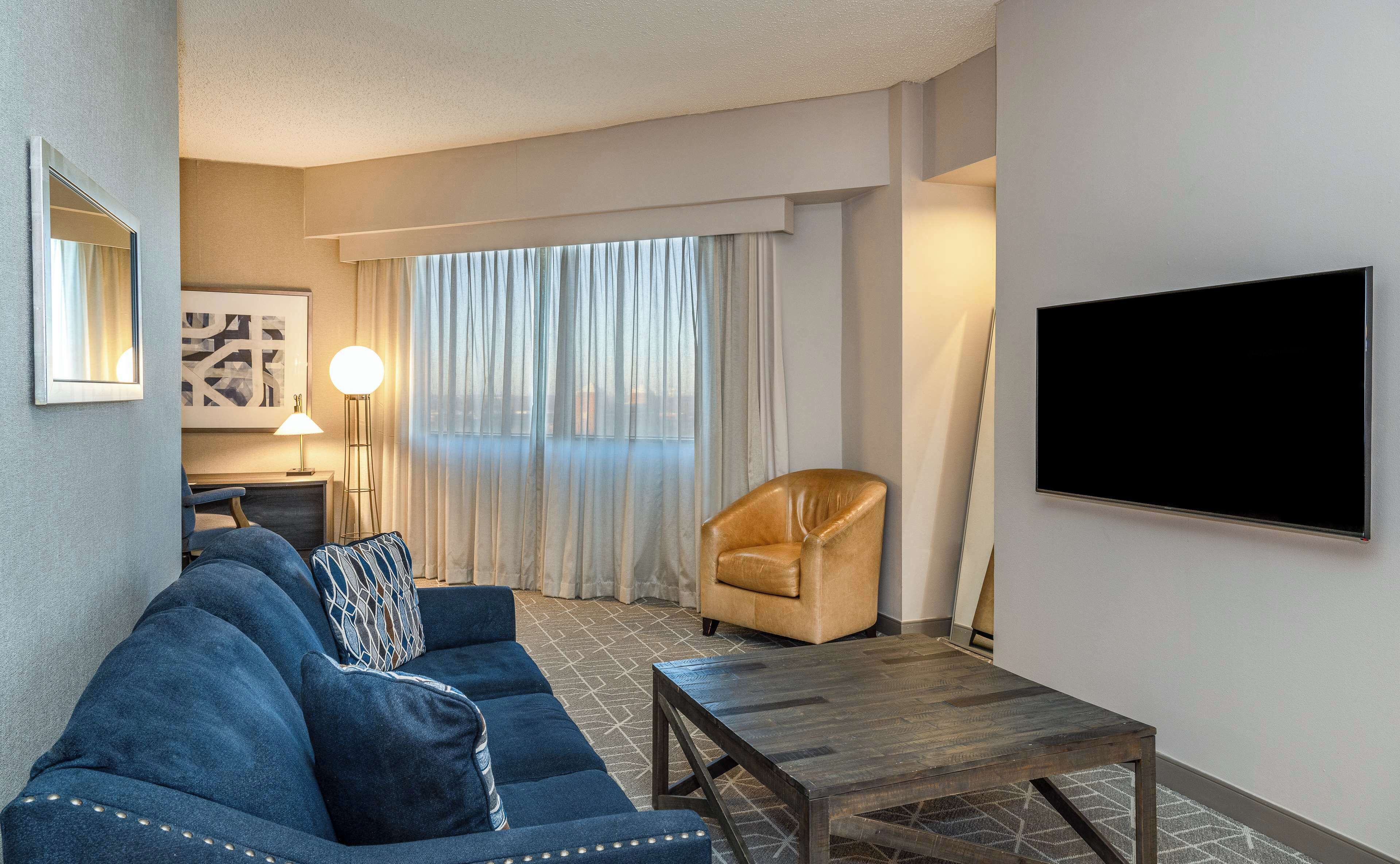 Une chambre d’hôtel moderne équipée d’un canapé, d  ’un fauteuil et d’un téléviseur à écran plat fixé au mur.