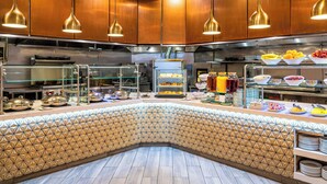 A modern kitchen with stainless steel appliances, a buffet counter with various food items, and geometric patterned tiles. - Hilton Richardson Dallas (Richardson)