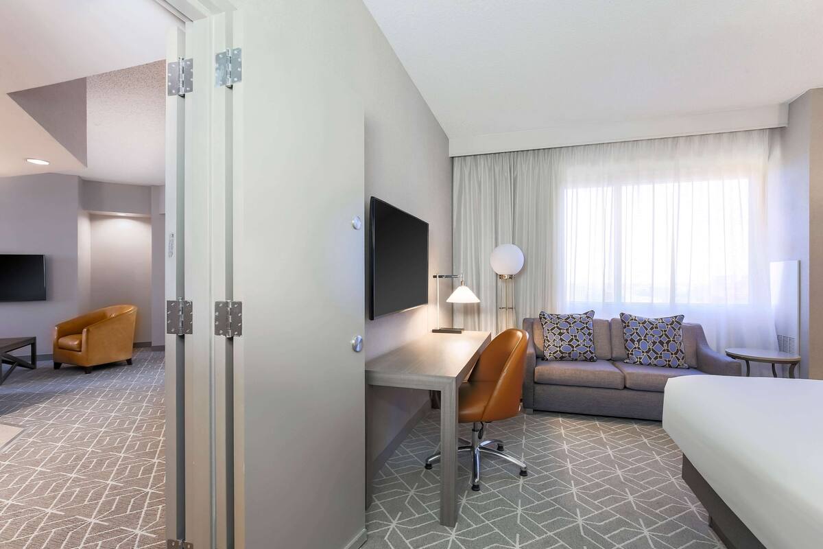 Quarto de hotel com cama, escrivaninha, cadeira, sofá e televisão.