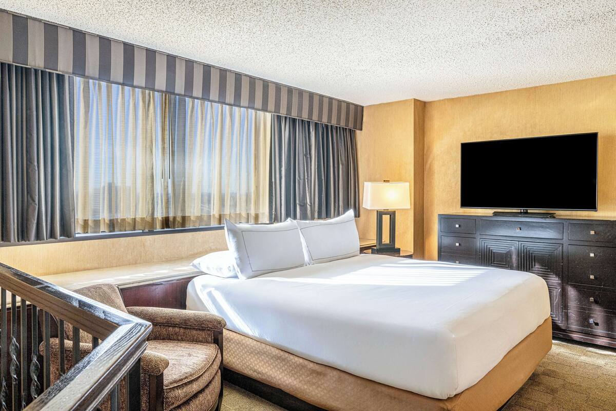 Quarto de hotel com uma cama grande, televisão de tela plana, escrivaninha e uma cadeira.