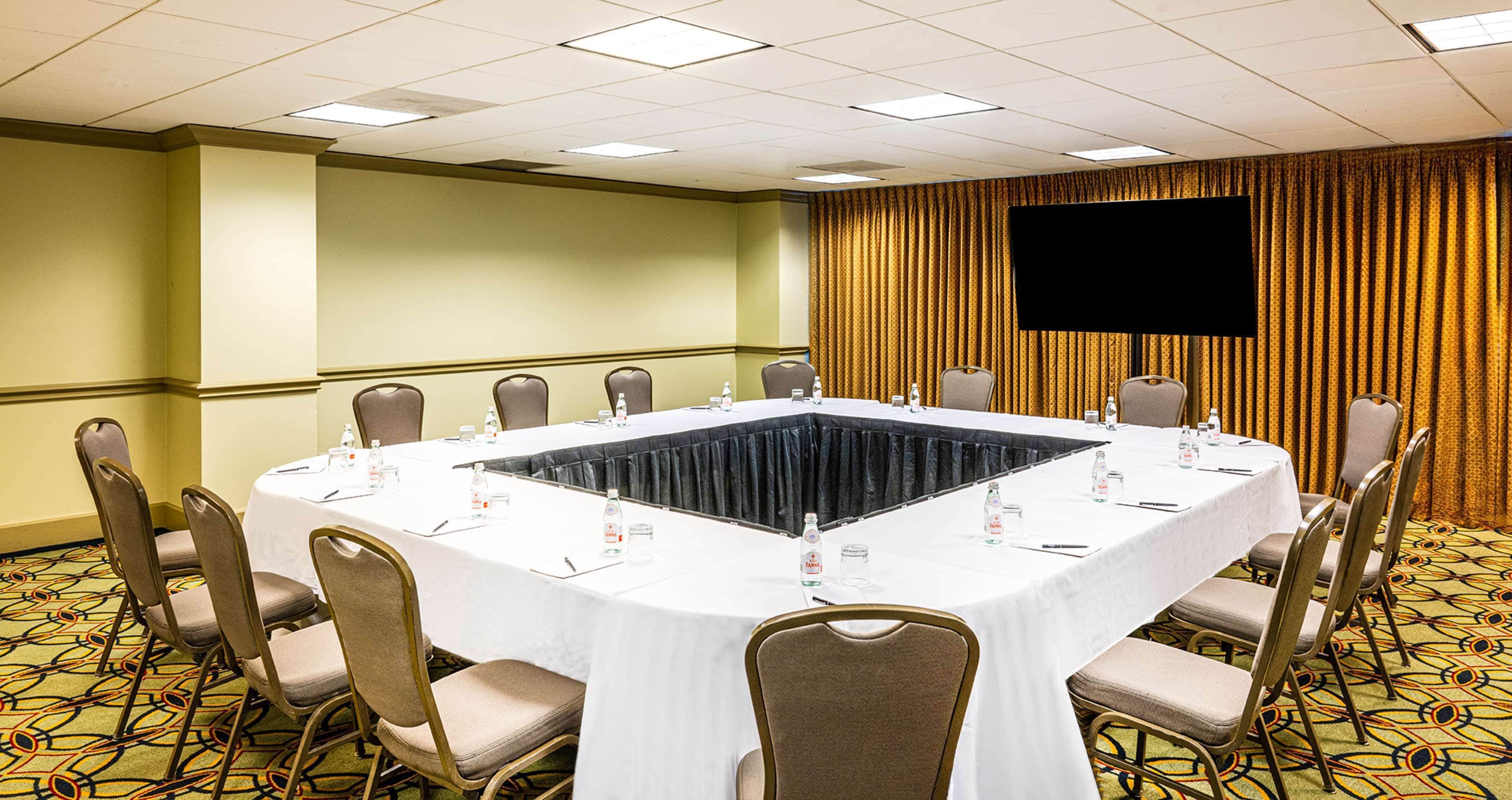 Une salle de conférence dotée d’une grande table ovale, de nombreuses chaises et d’un téléviseur à écran plat fixé au mur.