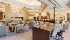 A modern hotel lobby with a central bar, seating areas, and a fireplace.