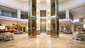 A spacious lobby with a high ceiling, marble flooring, and a central chandelier. There are seating areas with sofas and armchairs.