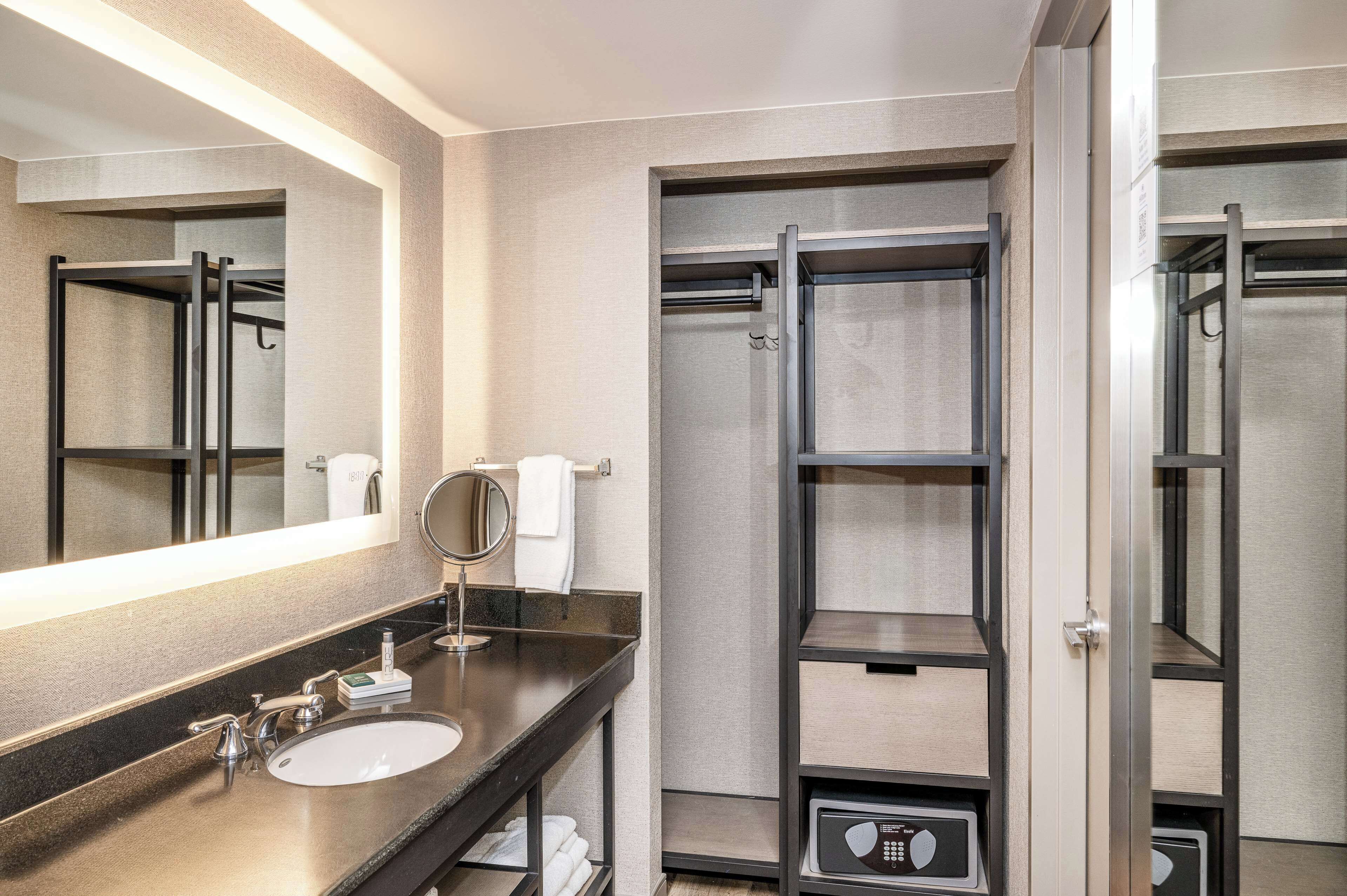 A modern bathroom with a large mirror, a sink, a shower, and a built-in shelf.