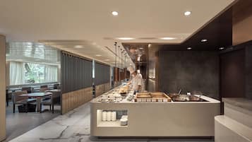 Un restaurante moderno con un chef preparando comida, suelo de mármol y una zona de estar con mesas y sillas.