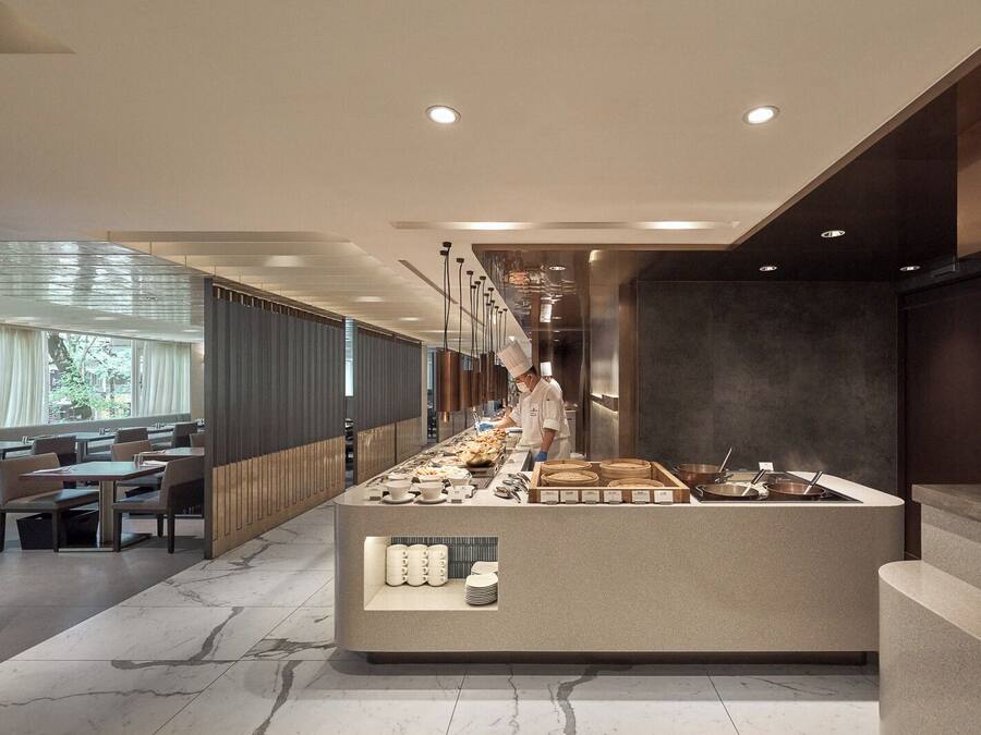Un restaurante moderno con un chef preparando comida, suelo de mármol y una zona de estar con mesas y sillas.
