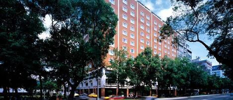 A multi-story hotel with a brick facade, surrounded by trees and a clear sky.