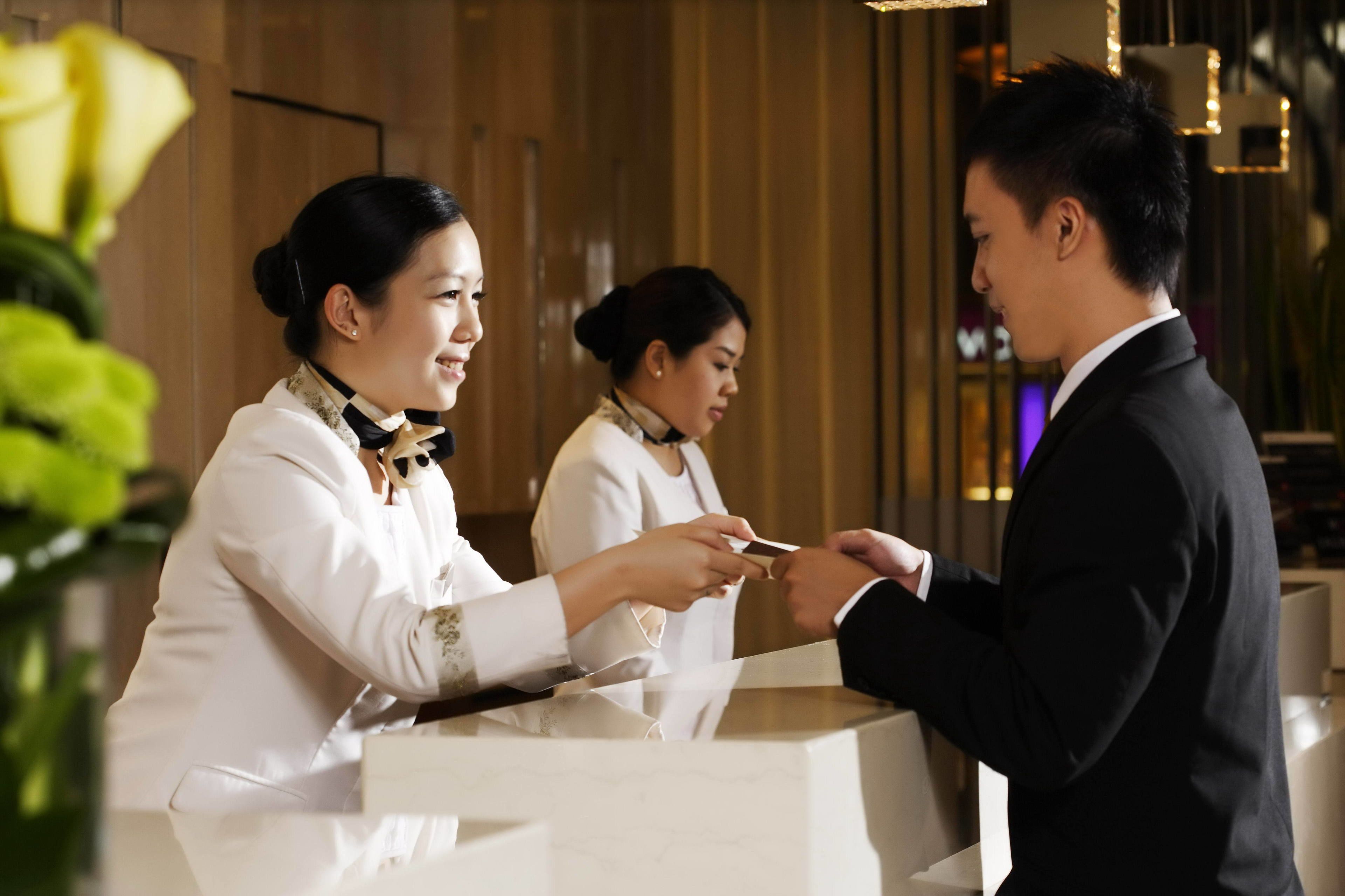 A reception area with a reception desk, a man and two women interacting, and a wooden interior.