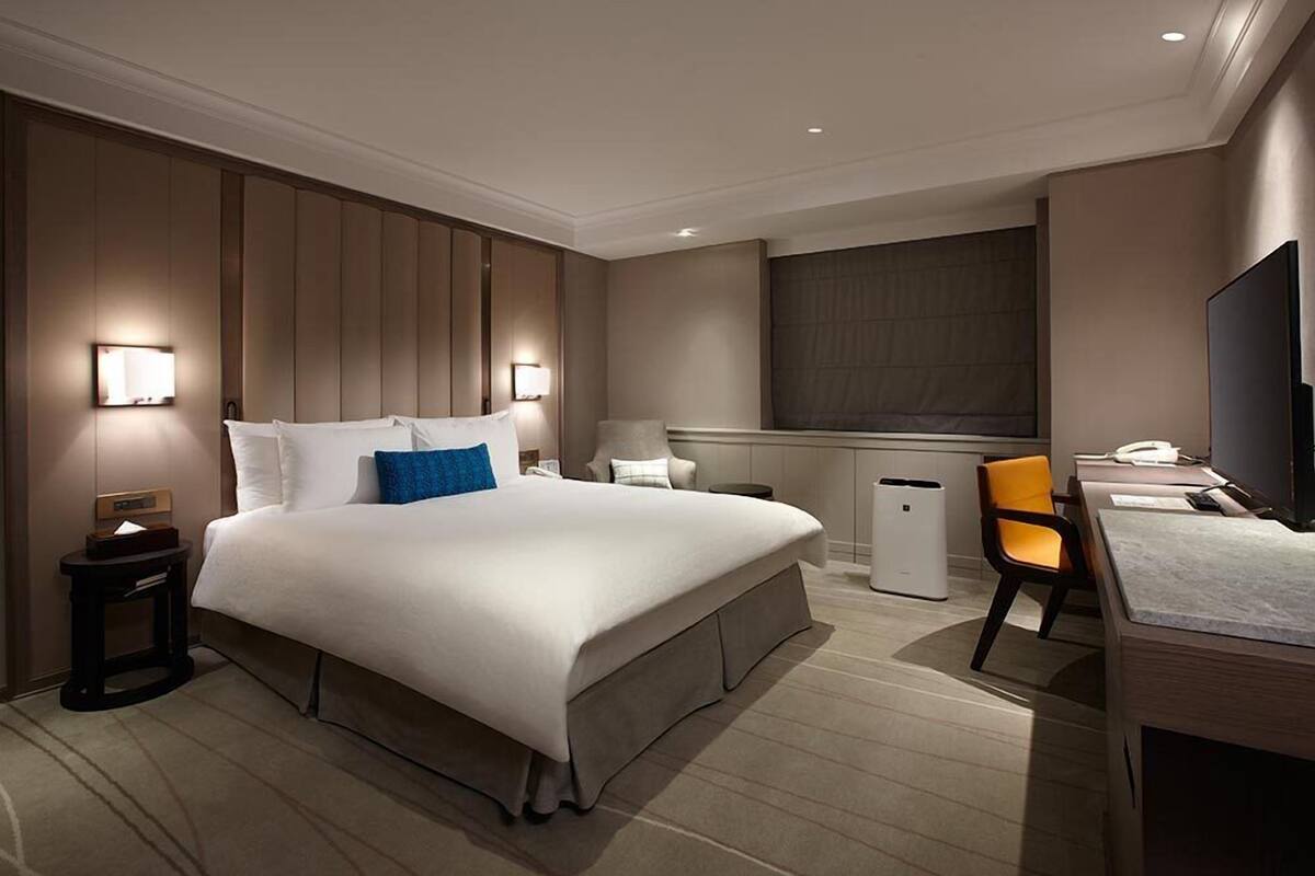 A hotel room with a large bed, bedside tables, a desk, a chair, a television, and a window.