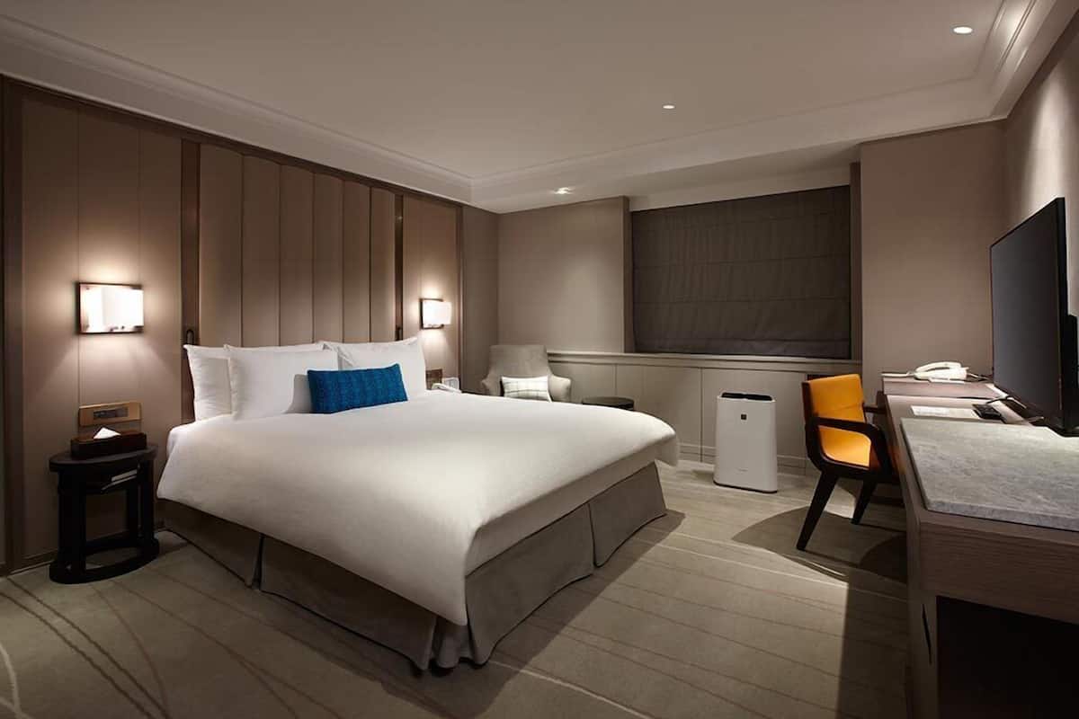 Habitación de hotel con una cama grande, mesitas de noche, un escritorio, una silla, un televisor y una ventana.