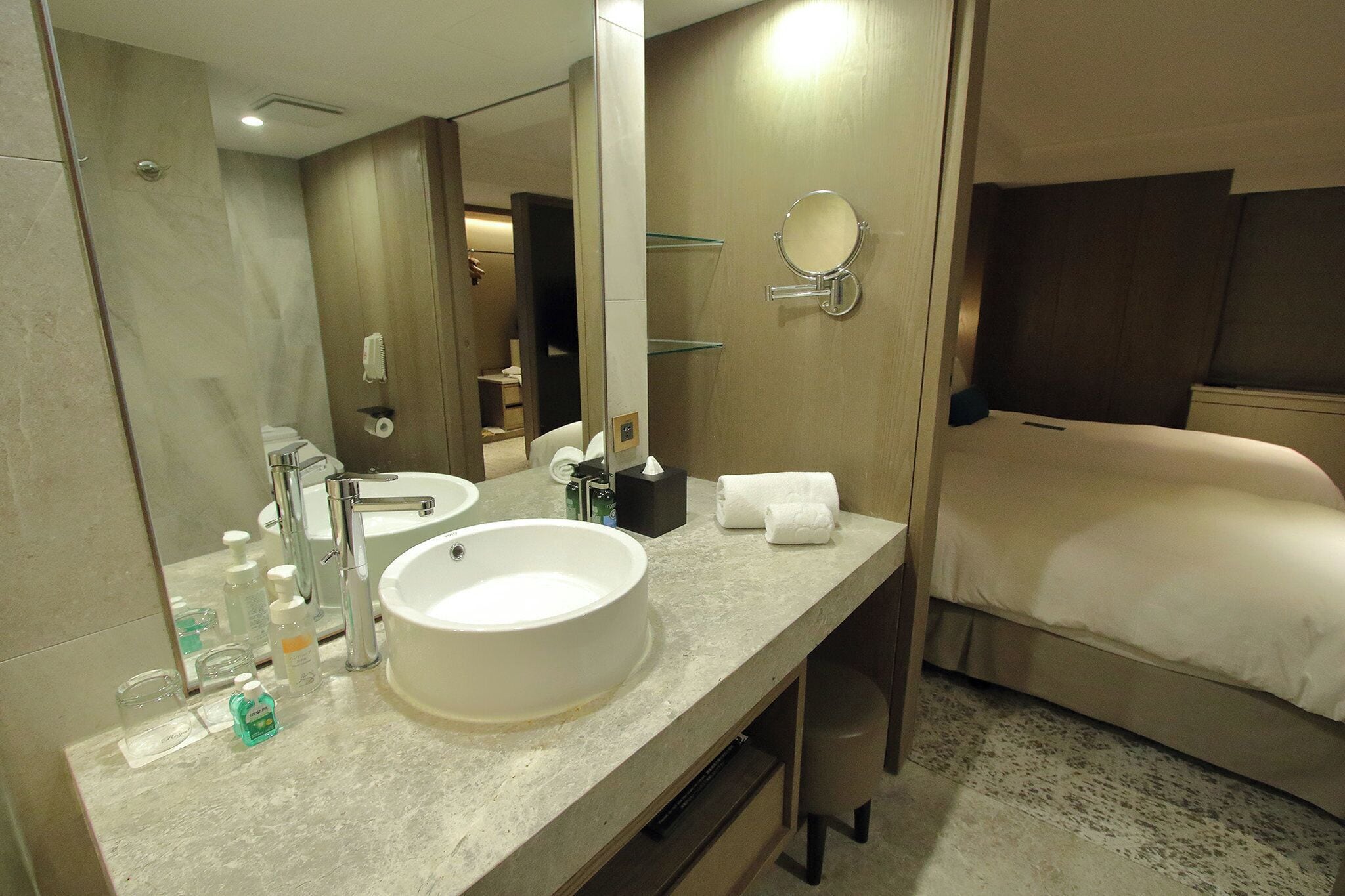 A modern bathroom with a large sink, two mirrors, a toilet, and a bed.