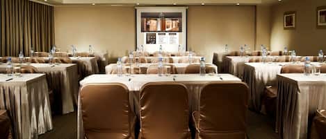 Un salón de conferencias con varias mesas, cada una con sillas y botellas de agua.