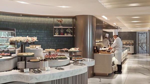 A modern hotel lobby with a marble reception desk, a decorative wall, and a chef preparing food in the background. - Hotel Royal - Nikko Taipei (Taipei)