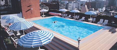 A rooftop pool with blue-striped umbrellas, lounge chairs, and a cityscape view.