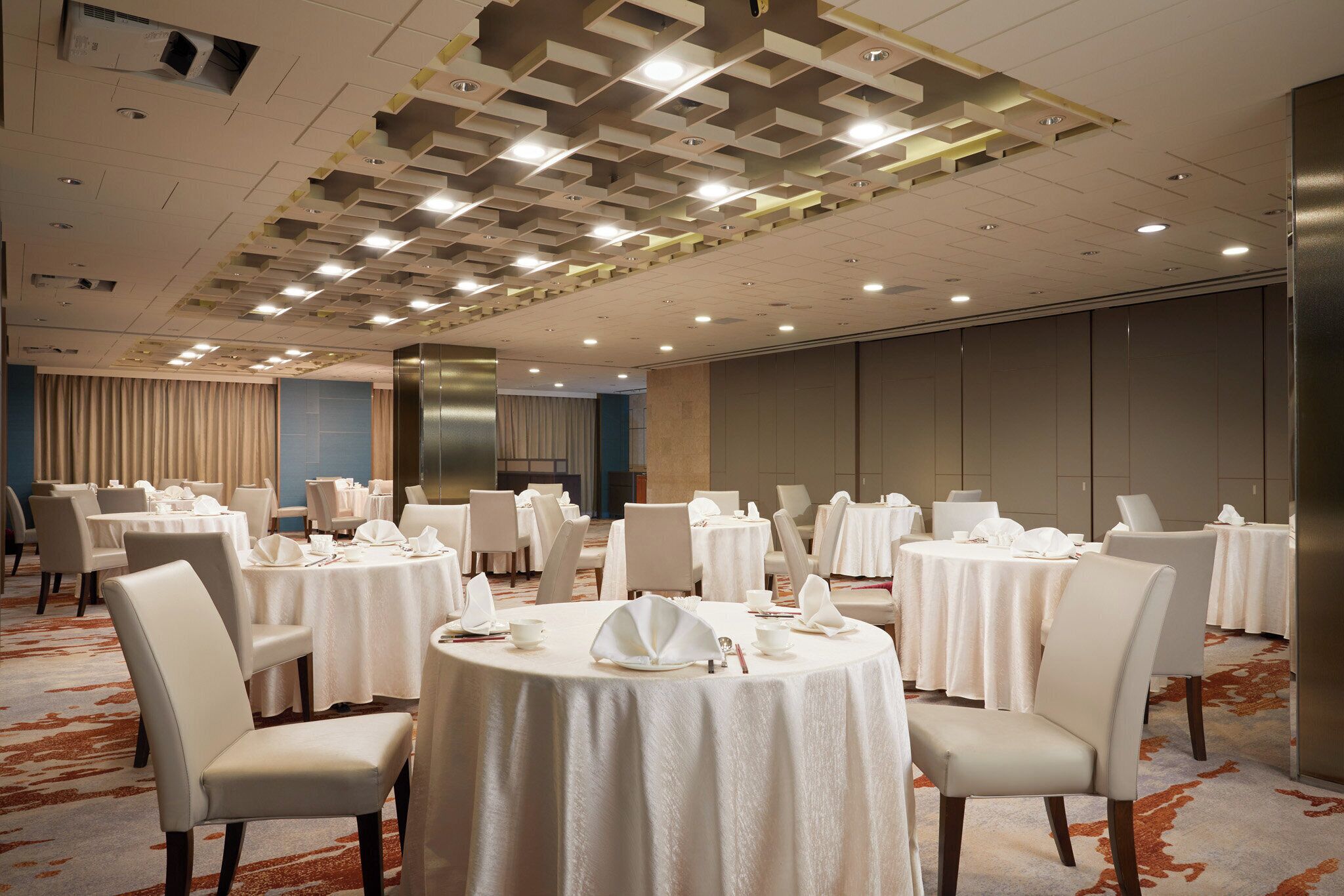 A hotel dining area with round tables, white chairs, and a patterned ceiling.