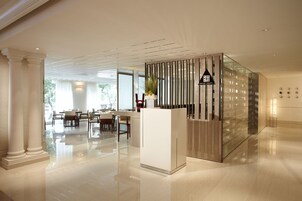 Uma área de recepção moderna com divisória de vidro, balcão de atendimento e um espaço de estar com mesas e cadeiras.