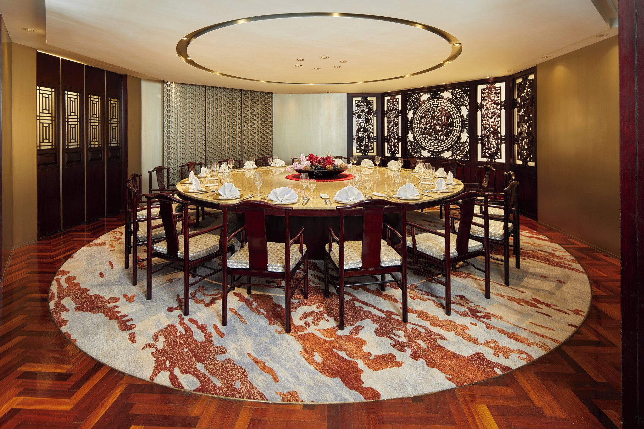 A round dining table with chairs, a floral centerpiece, and a patterned rug.
