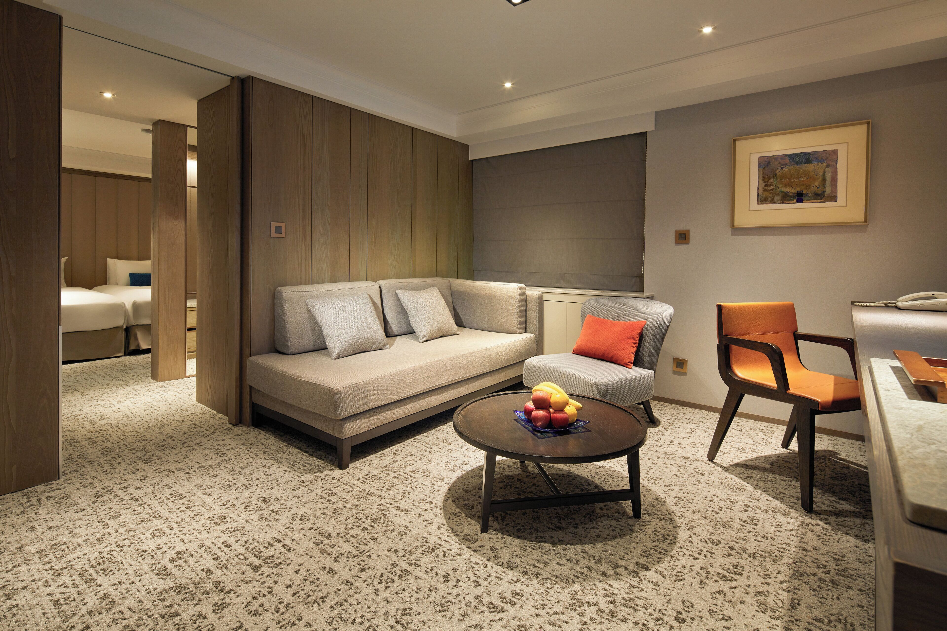 A modern living room with a sofa, armchair, coffee table, and a fruit bowl.