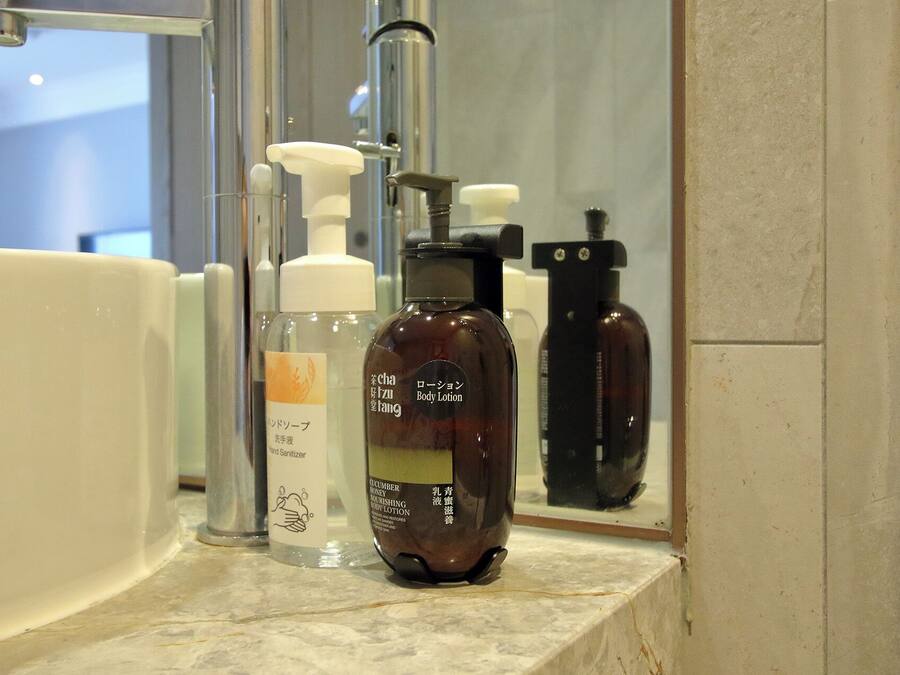A bathroom with a sink, a mirror, and various toiletries including a body lotion bottle.