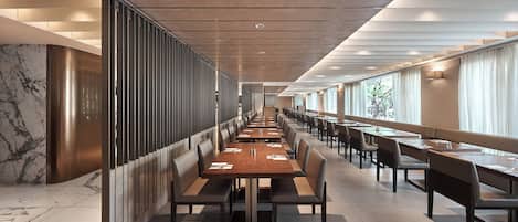 A long dining area with high tables and chairs, a marble wall on one side, and large windows on the other.