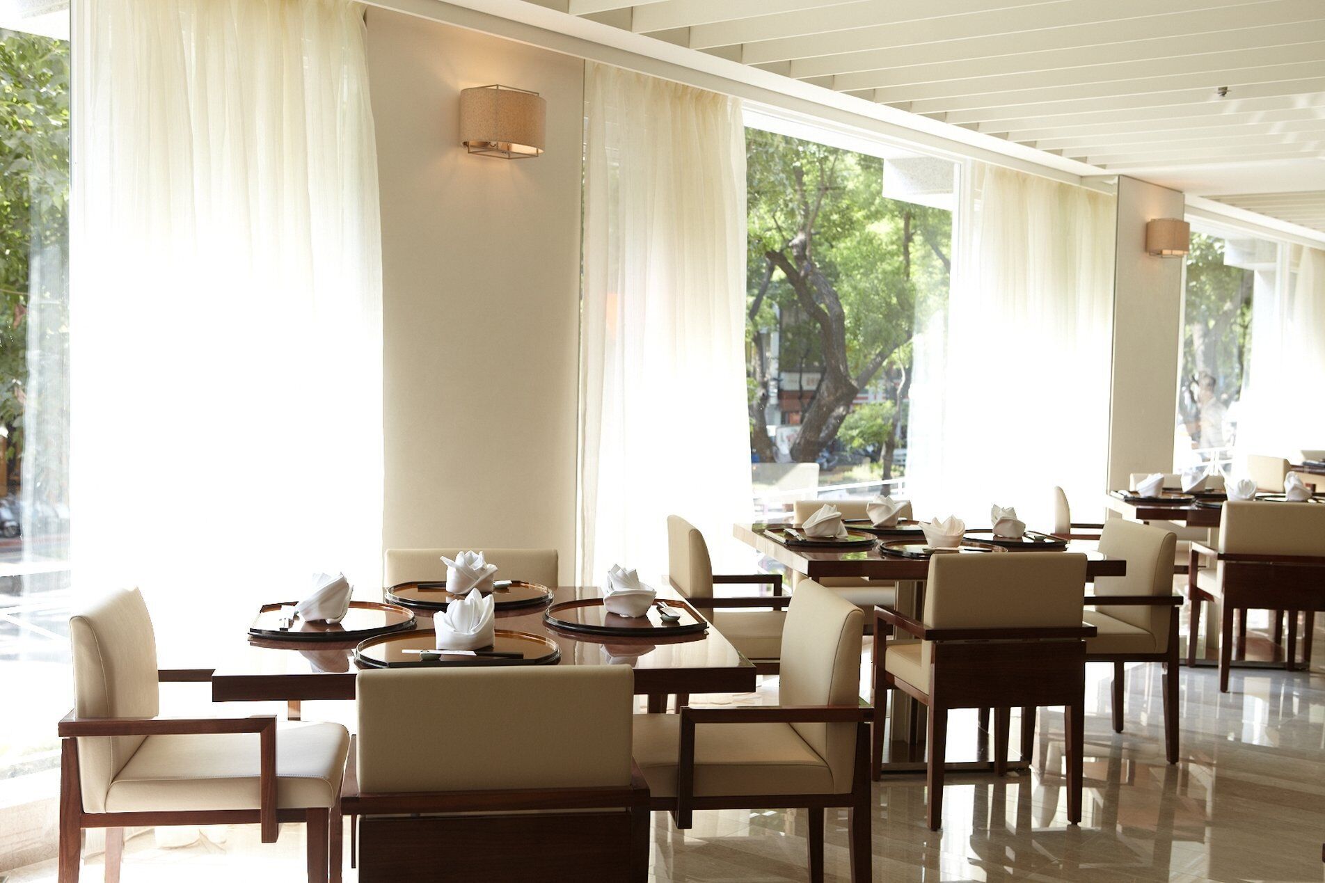 A restaurant with multiple tables and chairs, large windows with curtains, and a clean, modern interior.