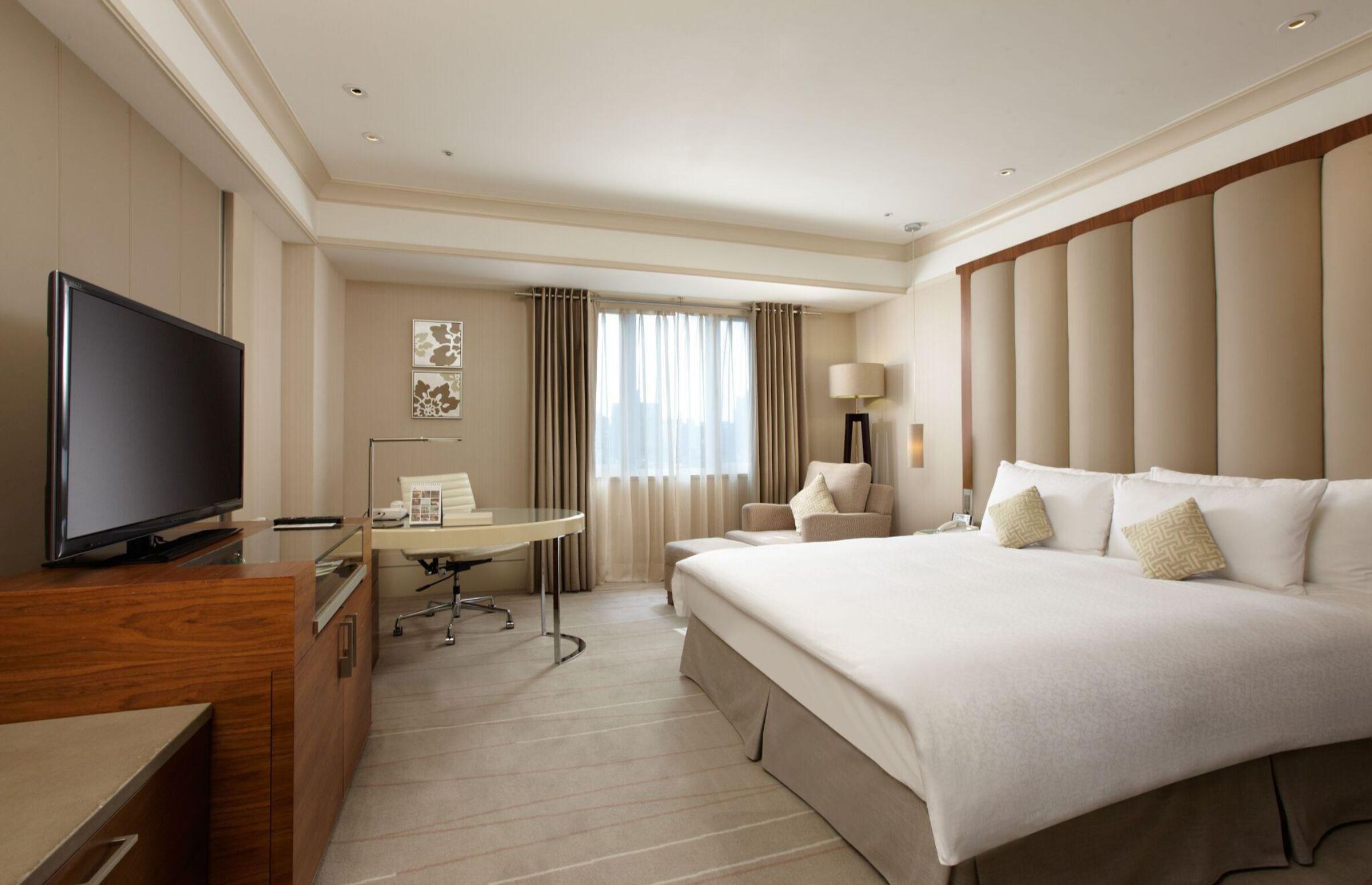 A hotel room with a large bed, a desk, a television, and a window with curtains.