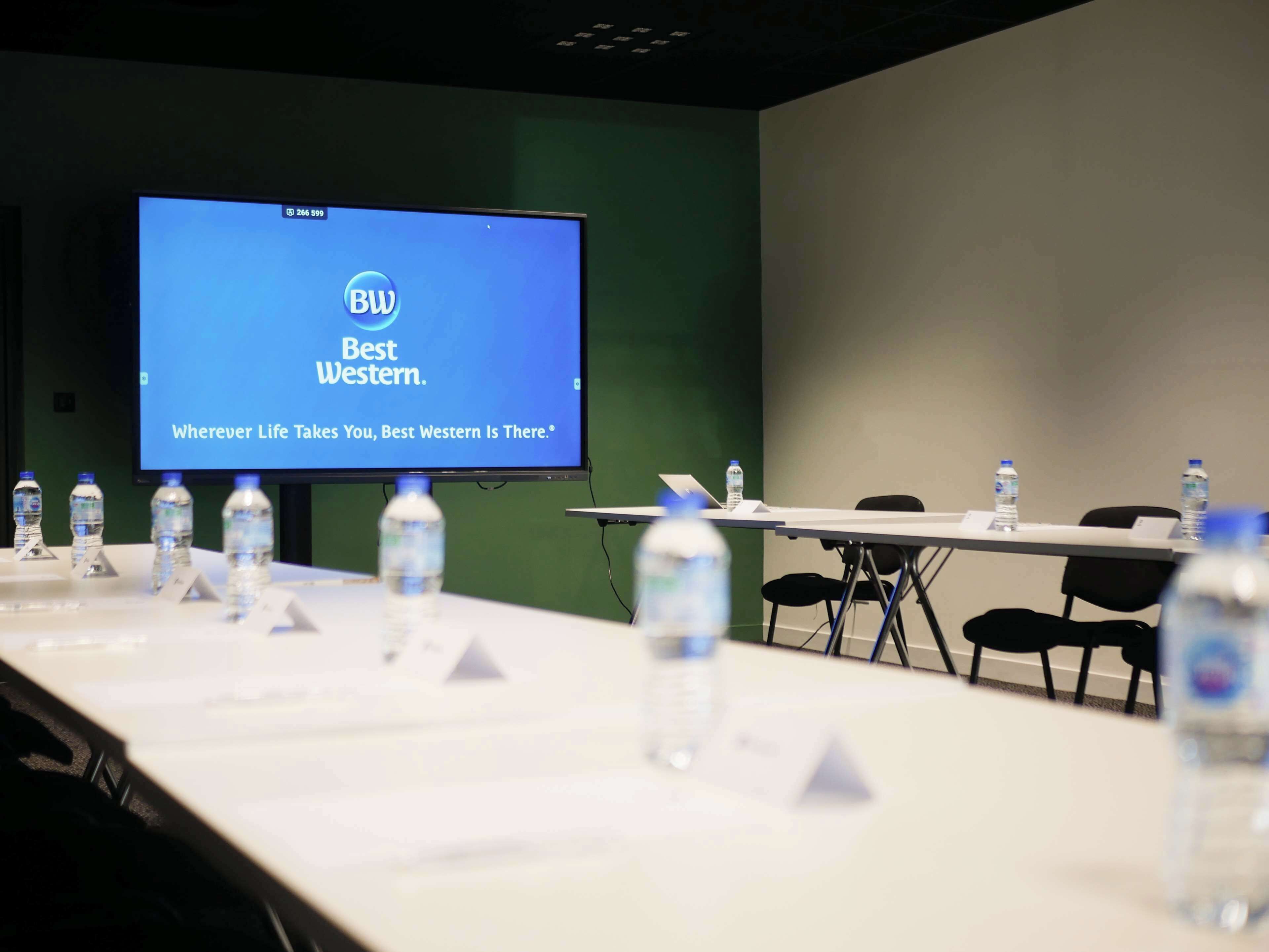 A conference room with a presentation screen displaying 'Best Western' branding, a long table with name tags, and water bottles.