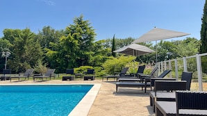 Une piscine entourée d’arbres et de verdure, avec des chaises longues et des parasols.