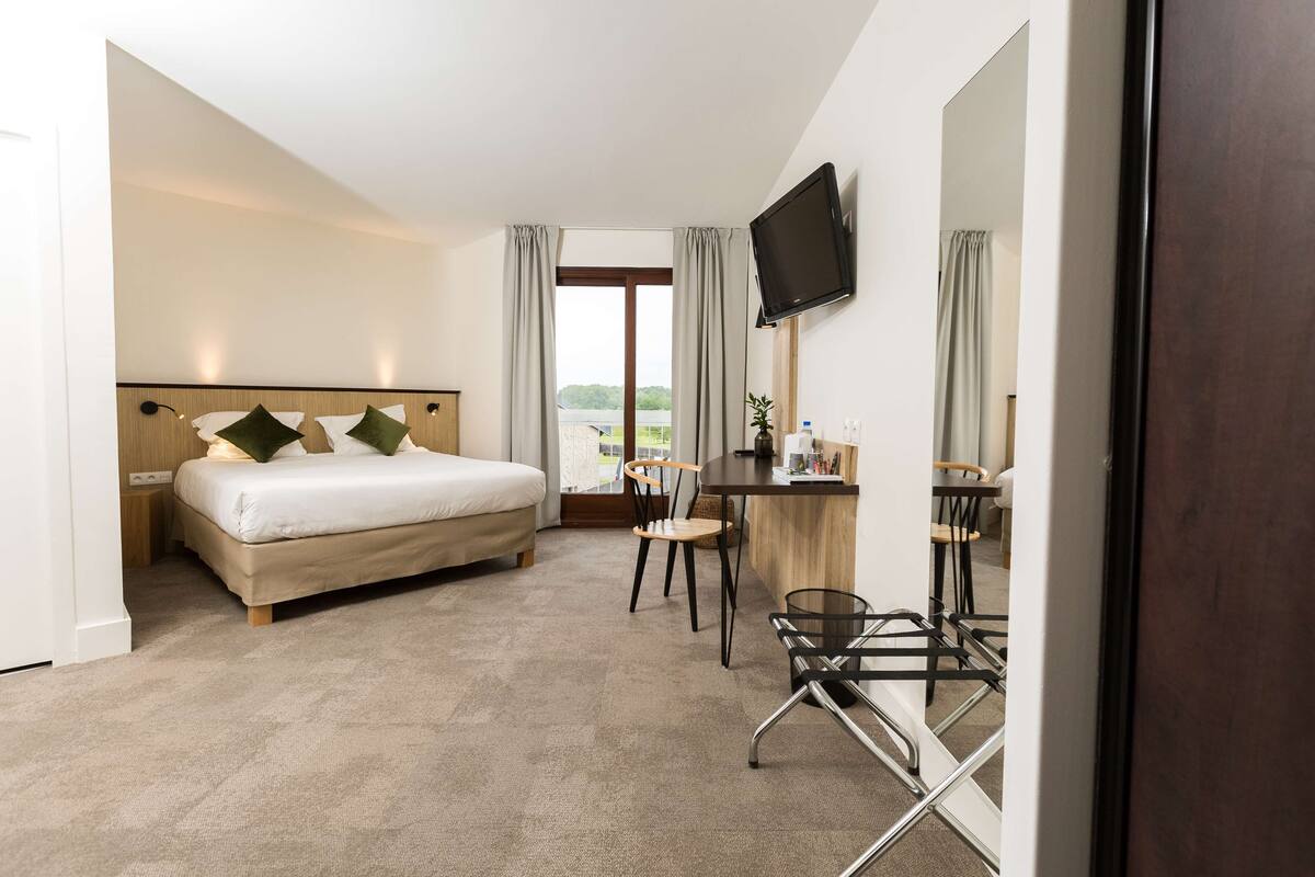 Une chambre d’hôtel équipée d’un lit, d’un bureau, d’une chaise, d’une télévision et offrant une vue sur l’extérieur.