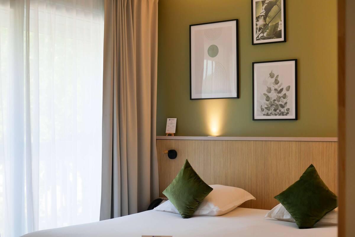 Une chambre d’hôtel avec un lit, des oreillers verts, une tête de lit et des œuvres d’art encadrées accrochées au mur.