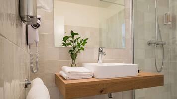 A modern bathroom with a glass shower enclosure, a wooden vanity with a white sink, a towel rack, and a hairdryer on the wall.