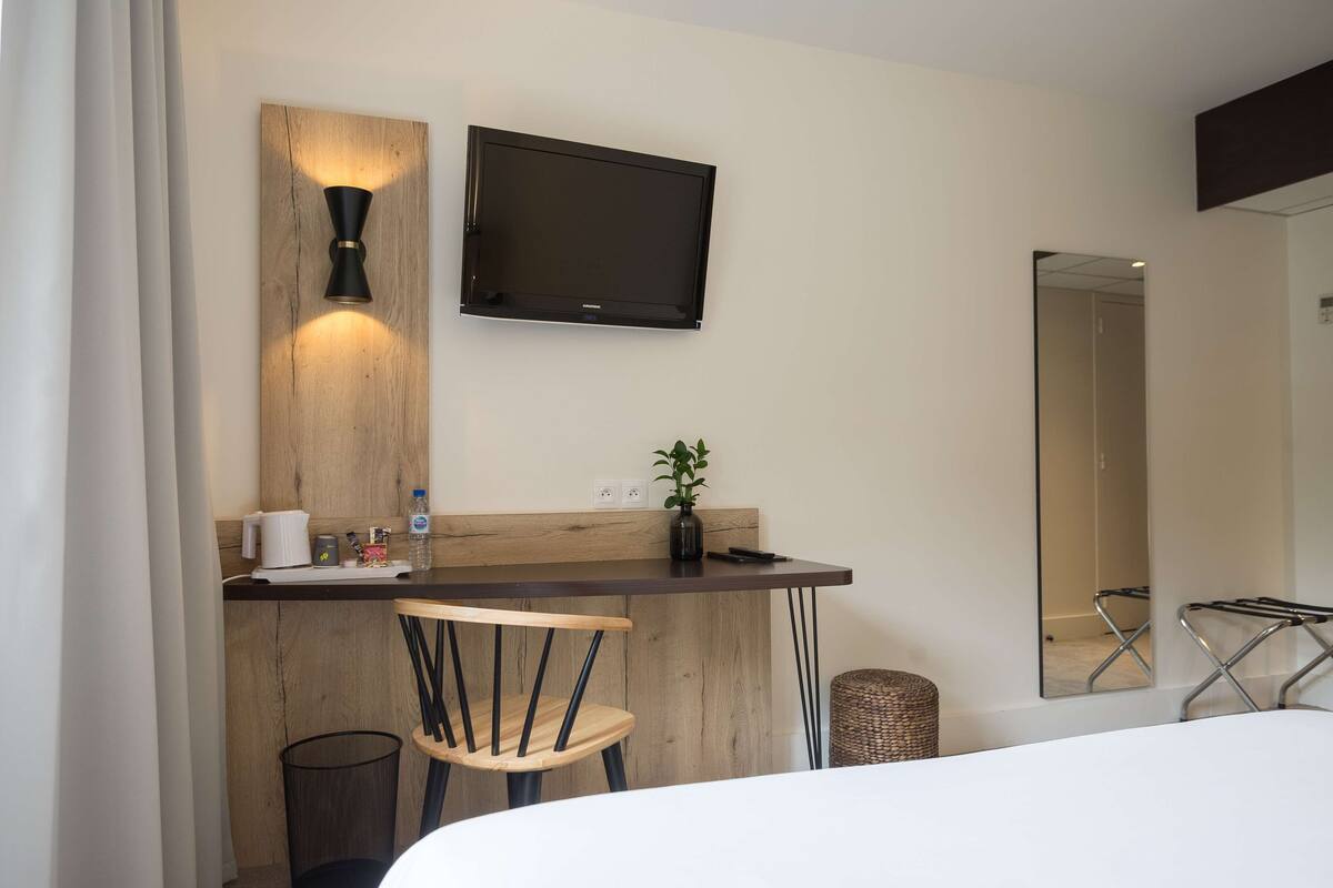 Une chambre d’hôtel avec un bureau en bois, une chaise, un téléviseur fixé au mur, une petite plante en pot et un miroir.