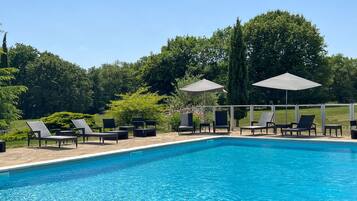 Une piscine entourée de verdure, avec des chaises longues et des parasols.