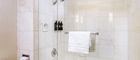 A modern bathroom with a glass-enclosed shower, a white bathtub, and a toilet.