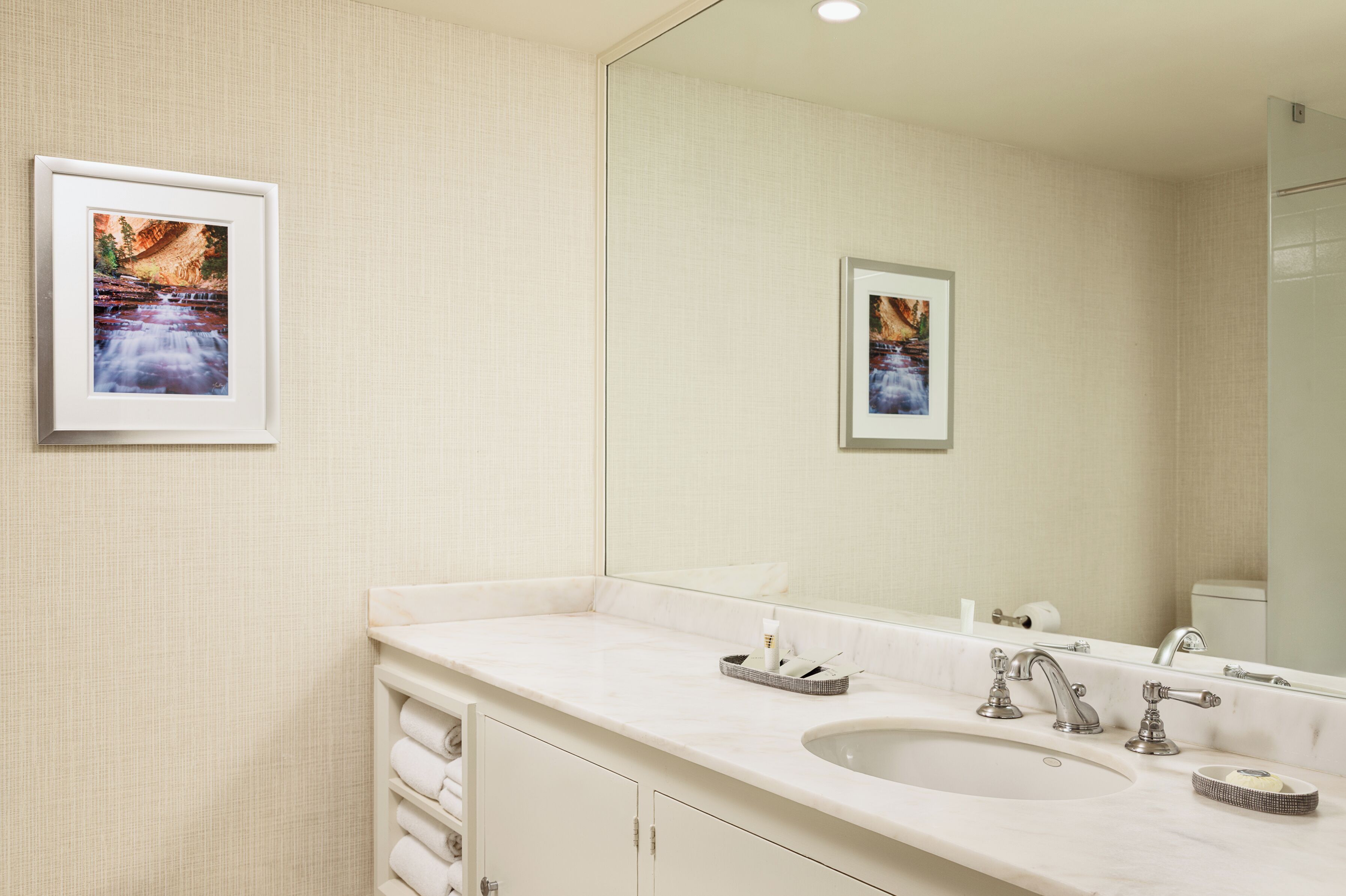 Une salle de bain avec un grand miroir, deux lavabos et des tableaux encadrés accrochés au mur.